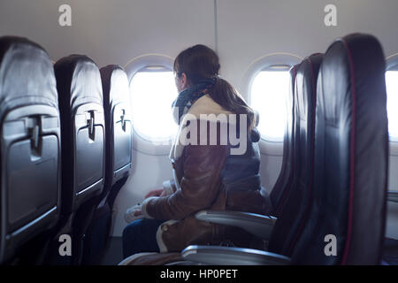Giovane donna è sul sedile del passeggero in aereo, guardando al di fuori Foto Stock