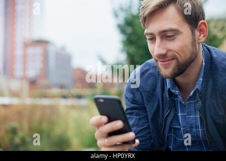 Uomo relax nel parco, guardando uno smartphone multimediale Foto Stock