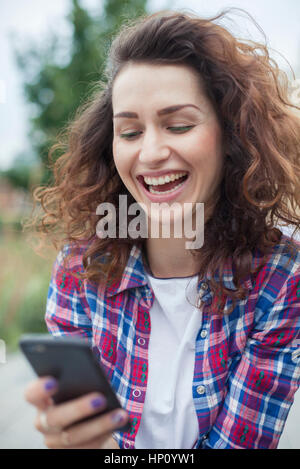 Giovane donna di ridere mentre la messaggistica di testo all'aperto Foto Stock