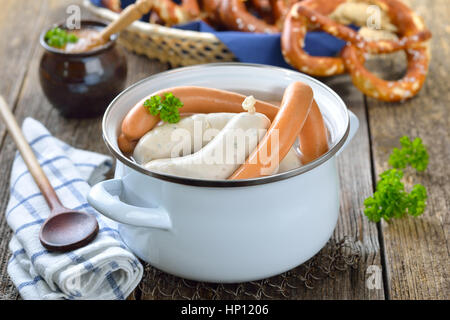 Bavarese a caldo le salsicce bianche e wieners in smalto di un recipiente di cottura servita su un tavolo di legno con un fresco e salatini e senape dolce Foto Stock