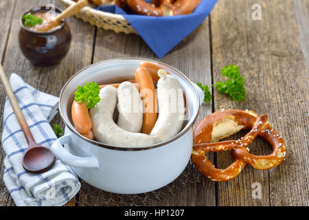 Bavarese a caldo le salsicce bianche e wieners in smalto di un recipiente di cottura servita su un tavolo di legno con un fresco e salatini e senape dolce Foto Stock