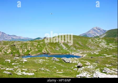 Gli escursionisti in prossimità di un lago naturale di "Plateau d'Emparis' con un piccolo aereo sopra di loro, Besse, Isere, Francia Foto Stock