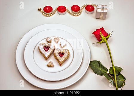 A forma di cuore ad Almond Linzer cookies su piastra bianca. Romantico set di rose rosse e luci di candela ffor anniversario di nozze, il giorno di San Valentino concetto Foto Stock