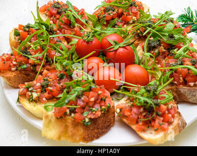 Stuzzicanti pomodoro antipasti italiani o bruschetta, su fette di pane abbrustolito baguette guarnita con pesto e insalata di rucola Foto Stock