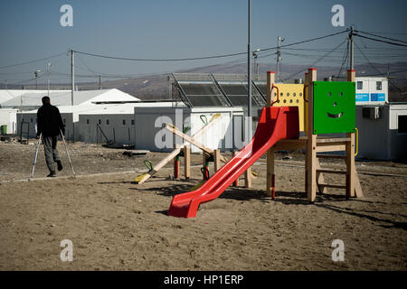 Tabanovce, Macedonia. Il 16 febbraio 2017. Nel transito temporaneo nel centro di Tabanovce un uomo ferito in una gamba passa da un parco giochi per i bambini rifugiati. Sono stare solo diverse dozzine di persone dopo la maggior parte dei rifugiati di origine siriana (nei pressi di un centinaio di persone sono state deportate indietro la scorsa settimana in Grecia dopo aver trascorso circa un anno nel camp. Adesso i rifugiati provenienti dal Pakistan, Afghanistan e del Maghreb (Marocco e Argelia) soggiornano in camp senza conoscere il suo futuro. Foto Stock