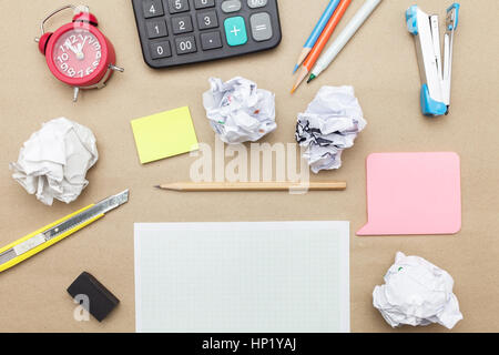 Concetto aziendale: Calcolatrice, spillatrice, orologio rosso, carta bianca vuota, carta accartocciata, post-it e matita colorata, matita, penna su sfondo di carta marrone Foto Stock