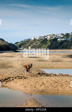 Un giovane ragazzo di scavare nella sabbia con la bassa marea sull'estuario di Gannel. Newquay, Cornwall, Regno Unito. Foto Stock