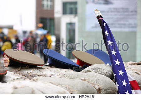 Una bandiera statunitense e cappelli militare dal periodo della guerra fredda al Checkpoint Charlie di Berlino. Foto Stock