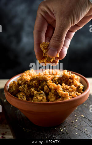 Primo piano di un giovane uomo di mangiare il couscous con le sue dita da una casseruola di terracotta collocati su una tavola in legno rustico Foto Stock
