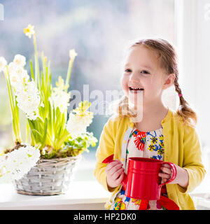 Ragazza carina prima di irrigazione fiori di primavera. Pasqua arredamento e decorazione. Bambino di prendersi cura di piante. Il capretto con acqua può. Bambino con fiore bas Foto Stock