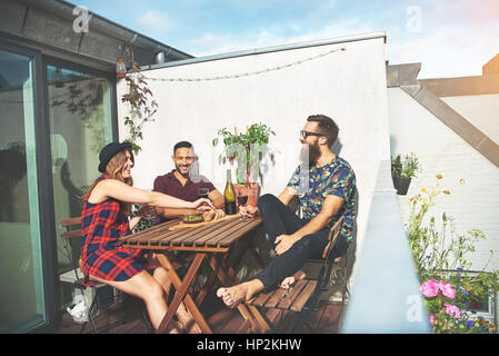 Uomo Barbuto con attraenti coppia giovane bere il vino a tavola in legno sul tetto in città europea Foto Stock