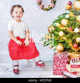 Carino piccolo bambino seduto nesxt dell albero di Natale Foto Stock