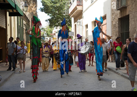 Un gruppo di musicisti palafitte vestiti con costumi di carnevale sfilano per le strade piene di turisti di l'Avana Vieja Cuba Foto Stock