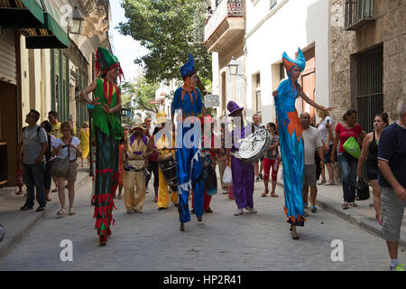 Un gruppo di musicisti stilted vestito in costumi di carnevale sfilano per le strade di Havna Vieja Cuba seguita da turisti Foto Stock