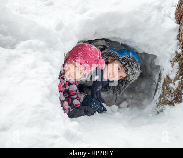 Felice un ragazzo e una ragazza che guarda fuori da una grotta di neve hanno reso in un cumulo di neve Foto Stock