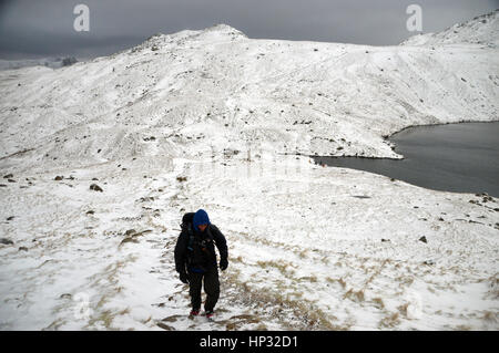 Maschio solitario Walker salendo nella neve per Esk Hause con angolo Tarn e la Wainwright Rossett Pike dietro ,Langdale,Parco Nazionale del Distretto dei Laghi, Foto Stock