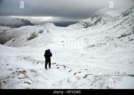 Un maschio solitario Walker salendo nella neve per Esk Hause con il Wainwrights Rossett Pike & Bow cadde dietro ,Langdale,Parco Nazionale del Distretto dei Laghi, Foto Stock