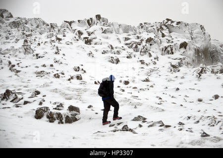 Lone Walker maschio di arrampicata in una tormenta di neve per la Wainwright Esk Pike da Esk Hause in Parco Nazionale del Distretto dei Laghi, Cumbria, Regno Unito. Foto Stock