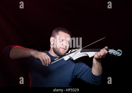 Il violinista barbuto gioca intensamente sul violino elettrico, isolata su uno sfondo nero Foto Stock