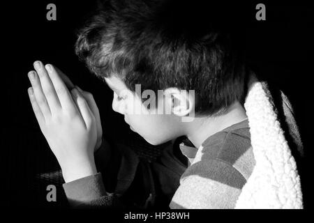 Giovane ragazzo in ginocchio a pregare prima di andare a dormire a occhi chiusi foto di Innocenzo la fede cristiana, concezione religiosa Foto Stock