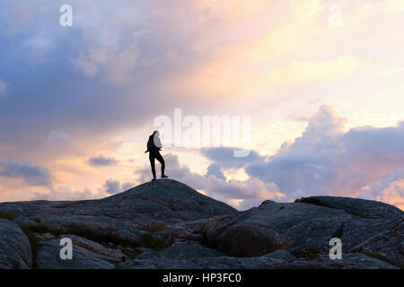 Un potente donna in piedi sulla sommità del de rocce vicino al faro di Lindesnes - Norvegia - durante il tramonto. Foto Stock