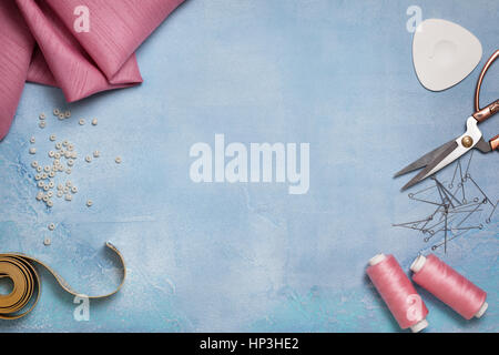 Strumenti per la cucitura: il tessuto, forbici, perni, misura di nastro blu su sfondo di calcestruzzo (vista dall'alto) Foto Stock