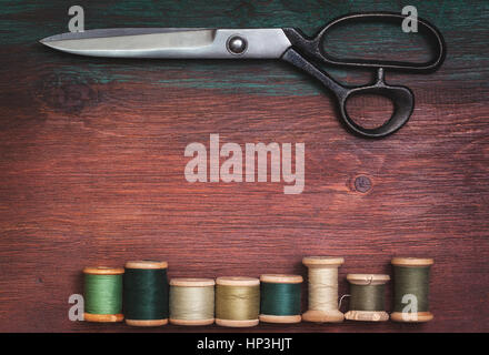 Forbici e vecchio thread sul vecchio sfondo in legno in stile vintage (vista dall'alto, tonificante) Foto Stock