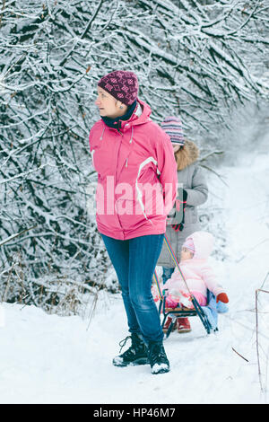 Donna tirando la slitta con la sua piccola figlia durante una passeggiata nel bosco Foto Stock