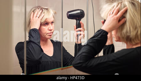 Donna matura utilizzato asciugacapelli nella stanza da bagno Foto Stock