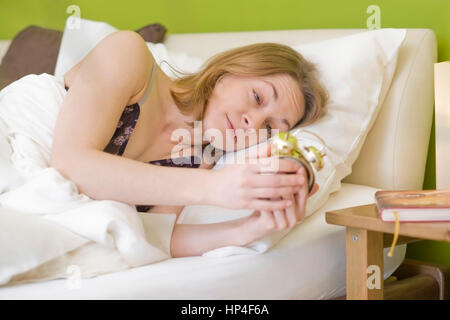 Modello rilasciato , Unausgeschlafene, junge Frau schaut auf den Wecker - donna svegliarsi con la sveglia Foto Stock