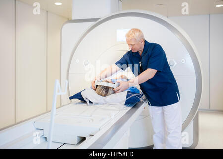 Radiologo mettendo le cuffie sul paziente sottoposto a scansione in MRI Foto Stock