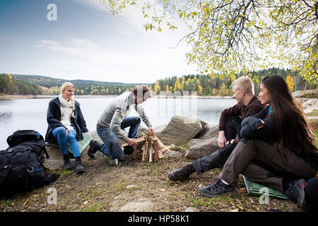 Amici guardando all uomo la preparazione di falò sulla camping sul lago Foto Stock