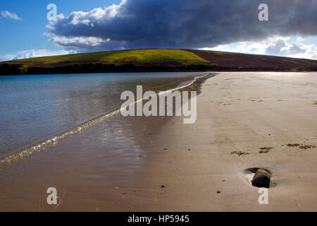 Una vista della spiaggia di Baia Waulkmill Orkney. Con una nube scura e cielo blu, illuminando una verde collina nella distanza. Con la luce spenta glinting th Foto Stock