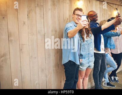 Numerose le persone felici gli uomini e le donne in piedi vicino a parete in legno con decorazioni e tenendo selfies. Spazio di copia Foto Stock