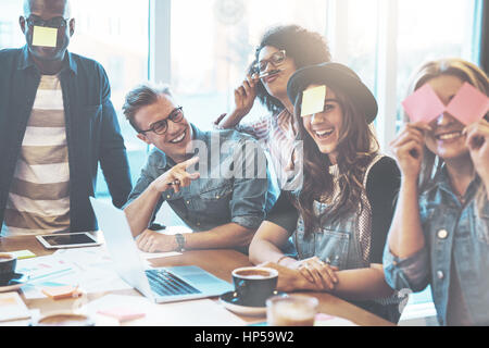 Gruppo di belle giovani al tavolo del bar con il computer portatile per divertirsi insieme giocando nome del gioco con note adesive per loro fronte, ridendo Foto Stock