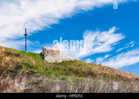 Croce e altare fatto di pietre sulla cima di una montagna, come sfondo un bel cielo blu con nuvole bianche Foto Stock