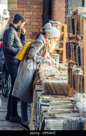 Una signora naviga attraverso i libri che sono in vendita su un mercato in stallo il passaggio pedonale coperto accanto al porto di Bristol nel Regno Unito. Foto Stock