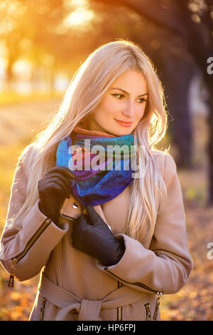 All'esterno Ritratto di giovane biondo caucasian donna che indossa il vestito di autunno, all'aperto nel parco sulla soleggiata giornata di caduta. Bella ragazza in cappotto beige e colorato Foto Stock