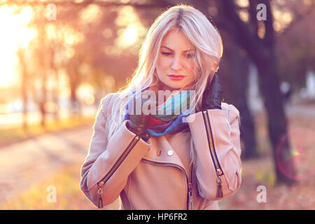 All'esterno Ritratto di giovane biondo caucasian donna che indossa il vestito di autunno, all'aperto nel parco sulla soleggiata giornata di caduta. Bella ragazza in cappotto beige e colorato Foto Stock