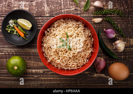 Noodle nella ciotola e ingredienti su uno sfondo di legno vista superiore Foto Stock