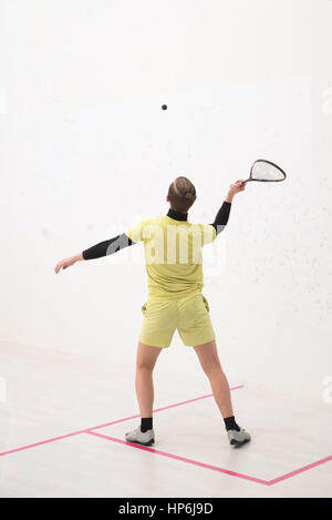 Vista posteriore del giocatore di squash di colpire una palla in un campo da squash. Giocatore di squash in azione. L'uomo gioca partita di squash Foto Stock
