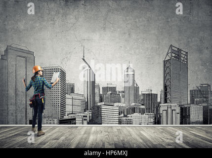 Vista posteriore di ingegnere di donna con la cartella e schizzi di progetto di costruzione sulla parete Foto Stock