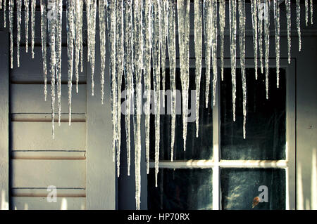 Ghiaccioli appesi da una grondaia della casa d'inverno. Foto Stock