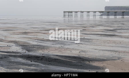 Mare del carbone lavato fino a Saltburn beach in inverno, e mostra anche il molo vittoriano e Warsett Hill Foto Stock