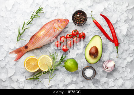 Rosso fresco pesce triglie con limone e rosmarino, avocado, peperoncino, pomodoro e spezie su superfici ghiacciate di sfondo di pietra Foto Stock