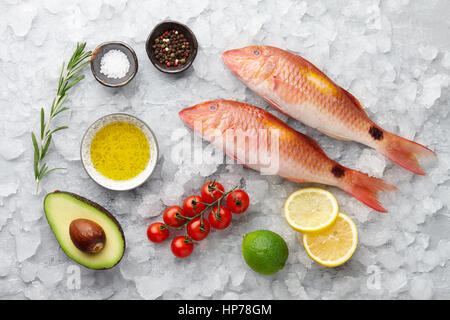 Rosso fresco pesce triglie con limone e rosmarino, avocado, peperoncino e spezie su superfici ghiacciate di sfondo di pietra Foto Stock
