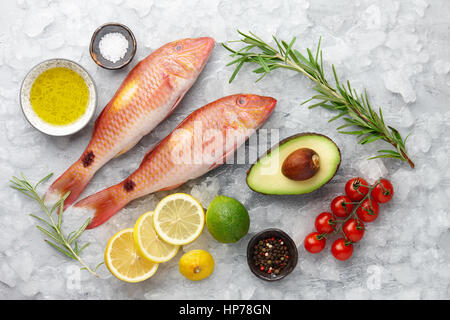 Rosso fresco pesce triglie con limone e rosmarino, avocado, peperoncino e spezie su superfici ghiacciate di sfondo di pietra Foto Stock