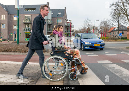 SOEST, PAESI BASSI - Jan 28: Uomo spingendo una donna su una sedia a rotelle a zebra crosssing in un villaggio olandese su Januari 28 a Soest, Paesi Bassi Foto Stock