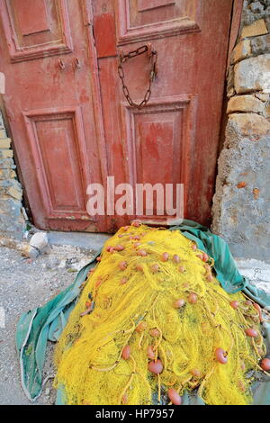 Pesca gialla net lasciato ad asciugare sul panno verde sul pavimento di backstreet nella centrale area del porto e di fronte a un dipinto di maroon la vecchia porta con catena arrugginita Foto Stock