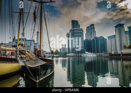 Barche, edifici per uffici e soggiorno di lusso a Londra Docklands sotto un cielo drammatico Foto Stock